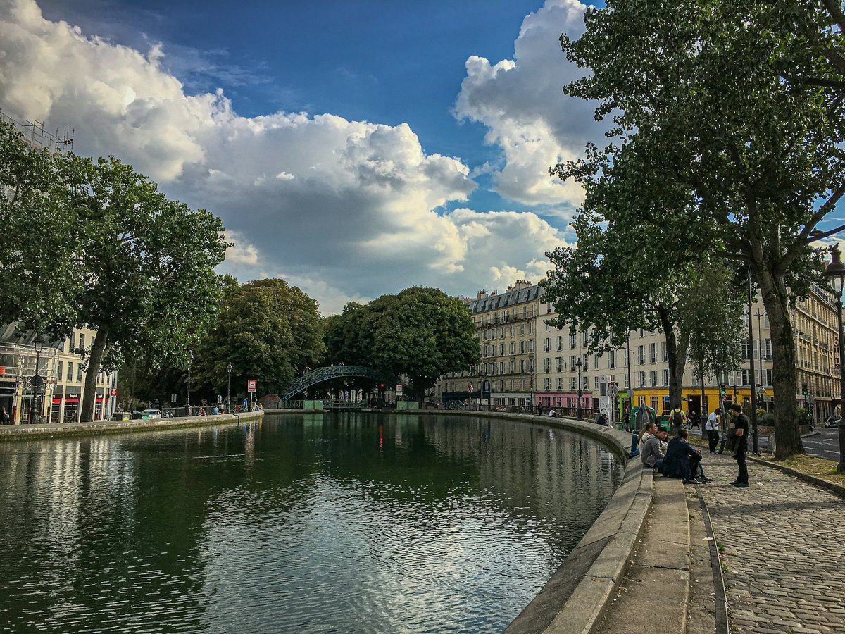 Canal parisien sous un ciel chargé de nuages, avec des promeneurs sur le trottoir