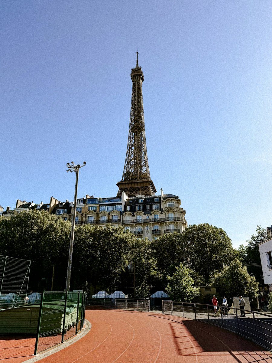 Piste d'athlétisme rouge au pied de la tour Eiffel, entre arbres et immeubles
