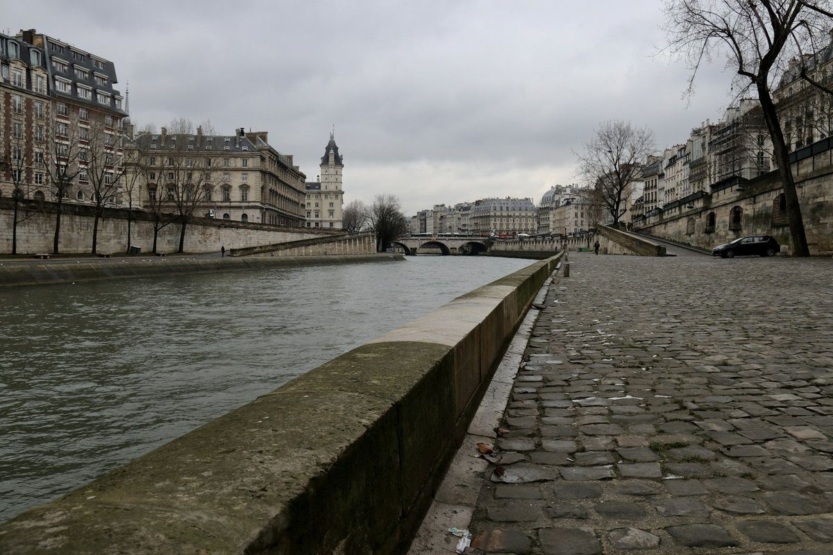 Quai pavé désert le long de la Seine, avec des immeubles de chaque côté du fleuve